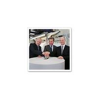 Drie mannen in pakken staan om een ronde tafel en leggen hun handen op een centraal object.