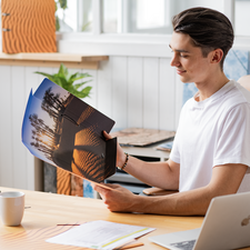 Ein junger Mann sitzt an einem Tisch und betrachtet eine Broschüre mit Bildern von Wüstenlandschaften und Palmen.