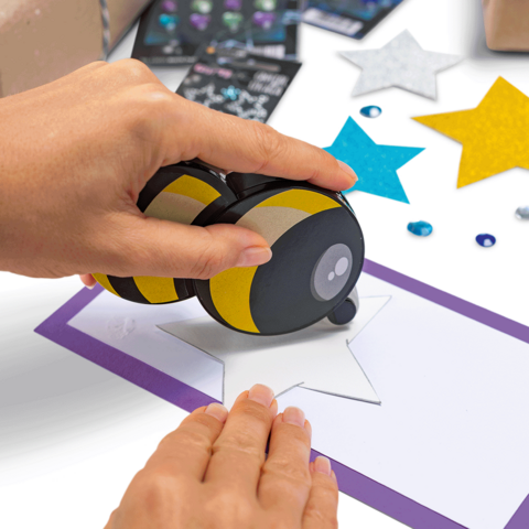 Een hand gebruikt een stempel om een ster op een vel papier te drukken, omringd door kleurrijke sterren en versieringen.