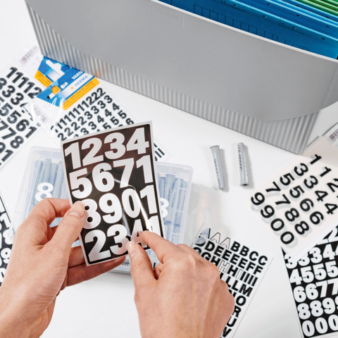 Handen houden een kaart met zwarte cijfers op een witte achtergrond, omringd door verschillende stickers en een organizer.