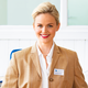 Een glimlachende vrouw met blond haar draagt een beige blazer en een witte blouse. Een naambadge toont 'Manuela Richter'.