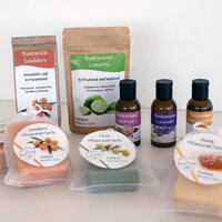 Labels op verschillende cosmetische producten: Doypacks met badmelk en badpoeder, bruine glazen flessen met badaroma, en plantaardige zeep met ronde etiketten in doorzichtige zakken, op een lichte achtergrond.
