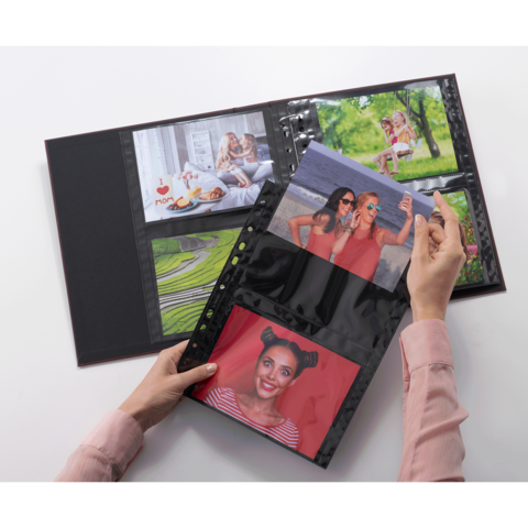 Eine Hand hält ein Fotoalbum mit mehreren Fotos, darunter Porträts von Personen und Landschaften, die in Klarsichthüllen eingelegt sind.