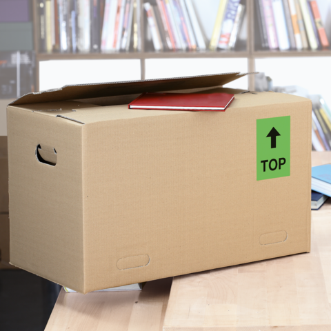 Ein Karton mit dem Aufkleber "FRAGILE", daneben ein graues Kuvert mit "URGEN!" und eine weiße Karte. Schere liegt daneben.