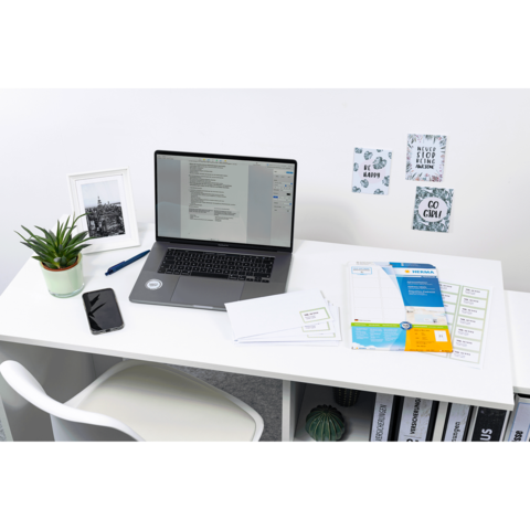 Schreibtisch mit Laptop, Smartphone, Pflanzen und Dokumenten. An der Wand hängen dekorative Notizen.