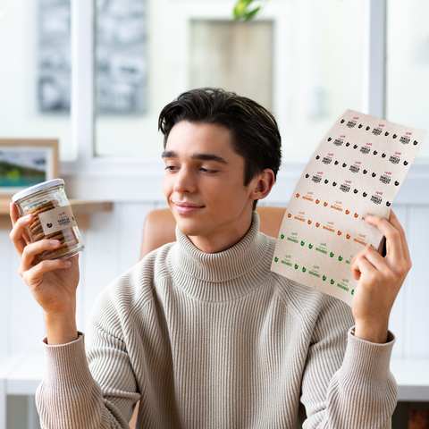 Een jonge man houdt in de ene hand een glas met snacks en in de andere hand een label met verschillende ontwerpen.